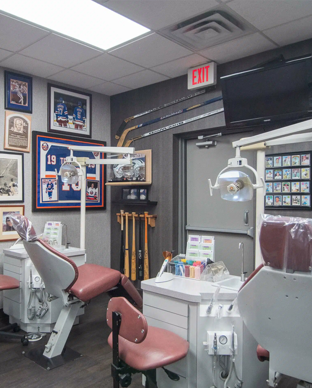 Orthodontic treatment room with dental chair, equipment, framed certificates, and professional displays on walls.